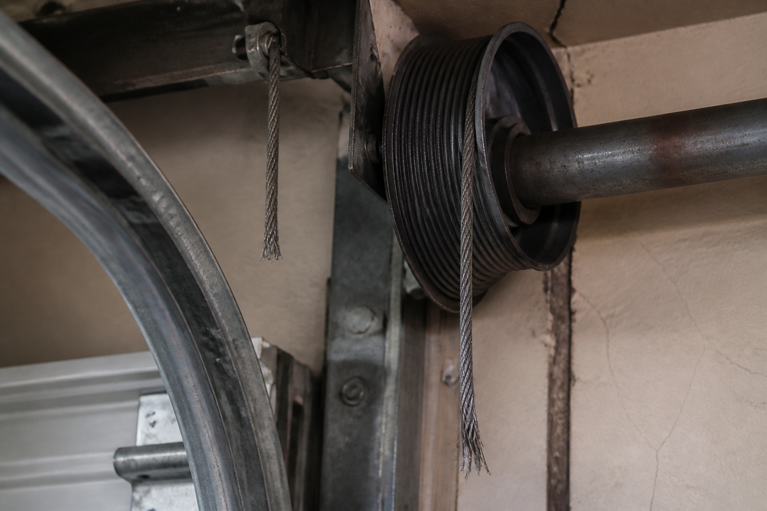 Frayed garage door lift cable with broken strands near the cable drum